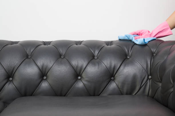 istock Employee hand in rubber protective glove with microfiber cloth cleaning luxury black leather chester sofa. Upholstered furniture. Early spring or regular clean up. Commercial cleaning company concept. 898277330