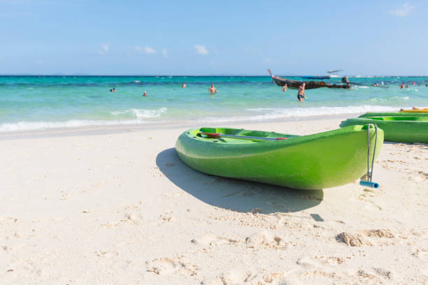 A green kayak on the beach,with blurred tourists on background, bali island,indonesia.