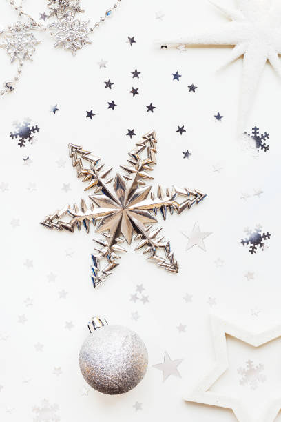 istock Christmas and New Year holiday background with decorations and light bulbs. Silver and white shining balls, white snowflakes and star confetti. Flat lay, top view. 898286966