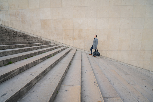 Profile shot of a businessman walking stairs up to work in the city of Paris.\nTravel success business industry concept\nShot in Paris, France