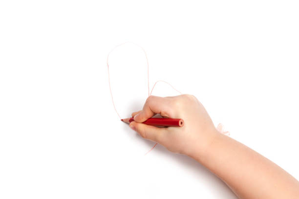 Child hand draws a crooked heart with a red pencil on white paper