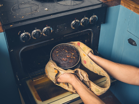The hands of a man is removing a burnt cake from the oven