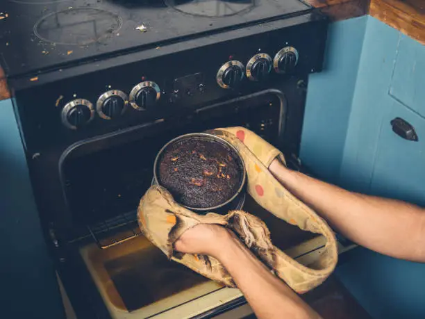 The hands of a man is removing a burnt cake from the oven