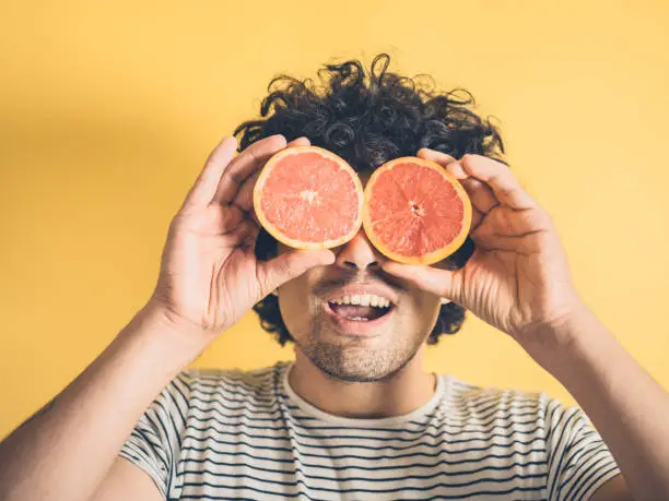 Photo of Silly young man using grapefruit as binoculars