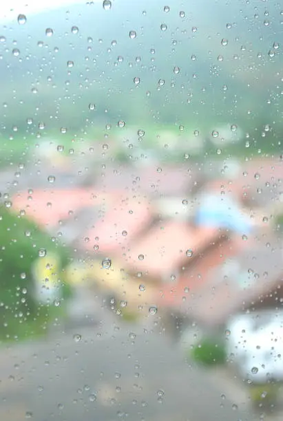 Water droplet on window after rain in summer season with background blurred of red roof 's house and moutain view, small lovely village in Swiss, europe.