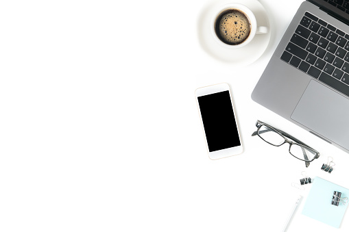 Desk with laptop, eye glasses, notebook and a cup of coffee isolated on white background. Top view with copy space.