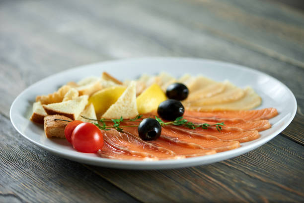 Close-up of white plate with the delicios appetizers set: fresh tomatoes,black olives, white bread pieces, smoked salmon slices and cheese.
