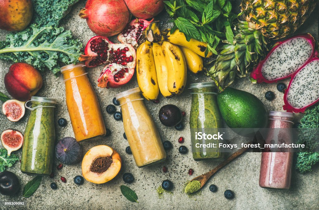 Colorful smoothies in bottles with fresh tropical fruit and superfoods Flat-lay of colorful smoothies in bottles with fresh tropical fruit and superfoods on concrete background, top view. Healthy, clean eating, vegan, vegetarian, detox, dieting breakfast food concept Juice - Drink Stock Photo