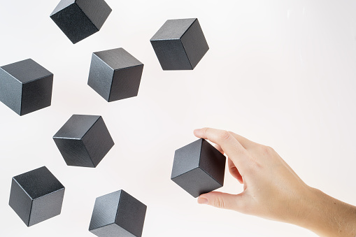 Black wooden cubes are floating. A woman's hand takes a floating cube.  Concept of creative, logical thinking. Abstract background with cubes with copy space. Floating shapes.