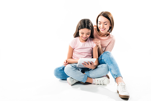 Mother and daughter sitting and looking at tablet on white