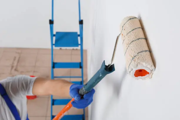 Photo of A man in gloves paints a wall with a roller for paint. Close-up. View from above.