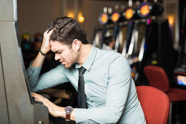Unlucky young man looking stressed and feeling sad after losing all his money in a slot machine at a casino