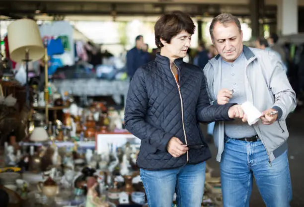 positive russian adult man and woman are looking antiquariat at the market of old things