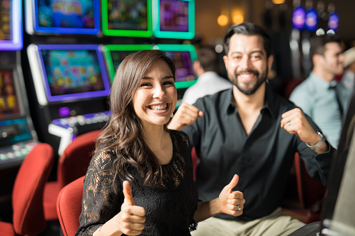 Cute looking couple going to the casino for a date and having some fun playing slots