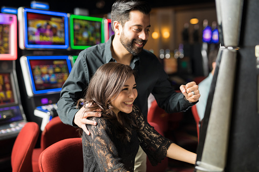 Portrait of an excited young Latin couple winning some money in a slot machine in a casino