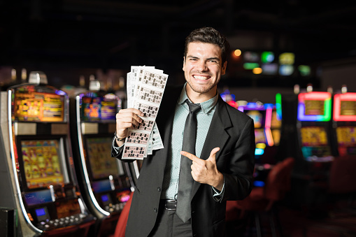 Portrait of a handsome young Hispanic man holding a bunch of lottery and bingo tickets and winning in a casino