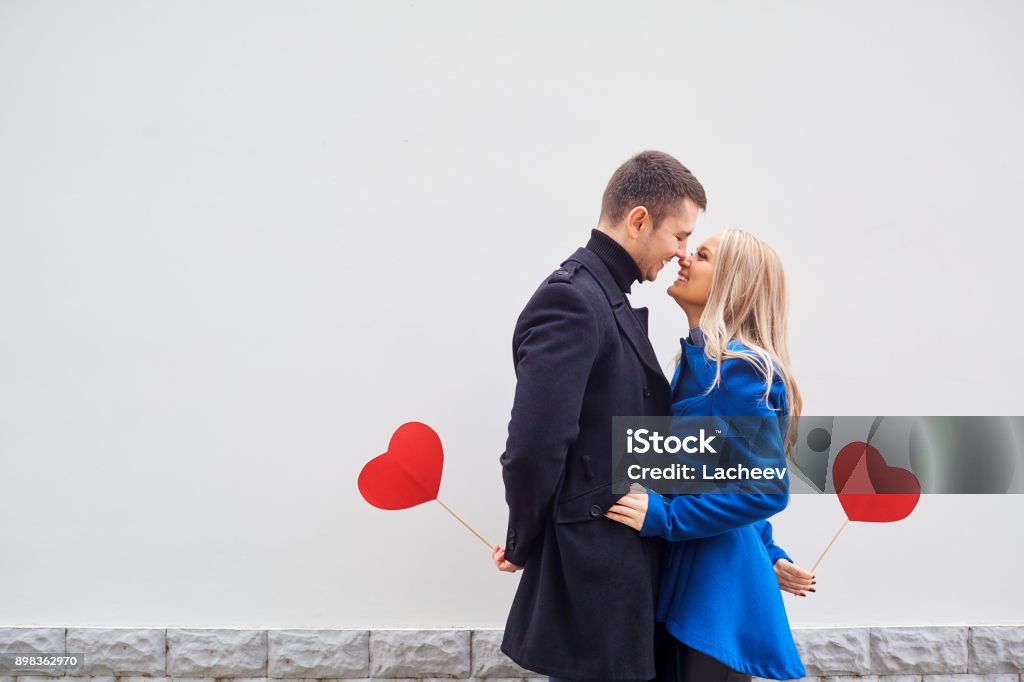 A loving couple in a coat with hearts in hands. A loving couple in a coat with hearts in hands on a gray background for text. Valentine's Day. Valentine's Day - Holiday Stock Photo