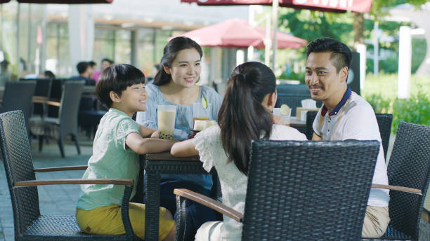 Chinese parents & kids taking break and enjoying drinks at outdoor cafe seat stock photo