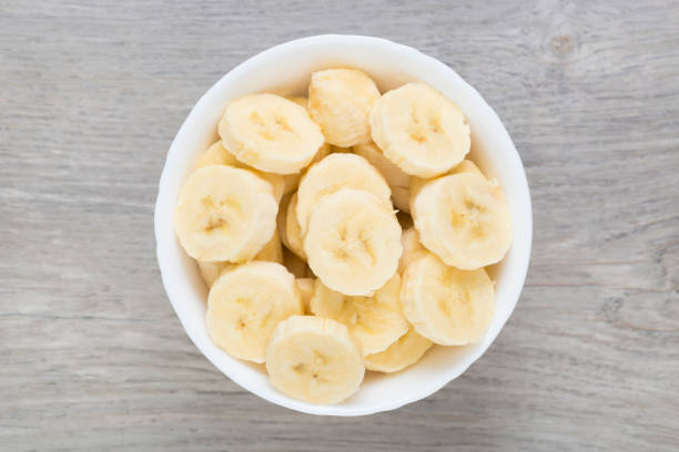 rebanar pedazos de plátano en tazón de fuente blanco. directamente sobre la vista. - peeled juicy food ripe fotografías e imágenes de stock