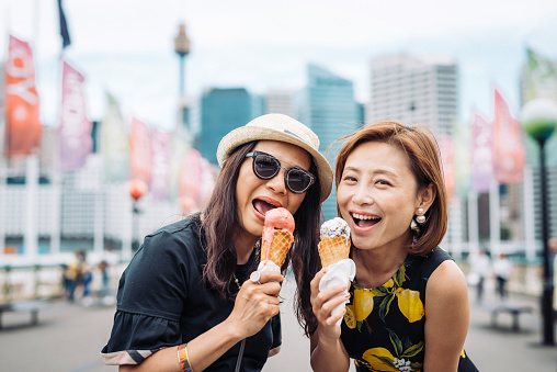 Cheerful Chinese mature women enjoying ice cream in Sydney, in summer. Two friends are traveling across Australia and having fun together