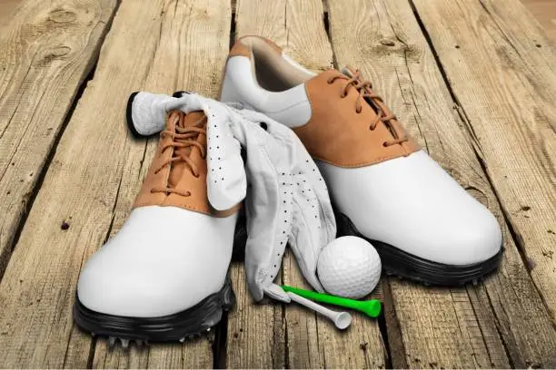Pair of golfing shoes, ball and tees on wooden background
