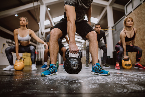 Group Of Men And Women Squatting With Kettlebells
