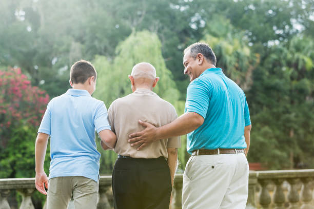 Multi-generation Hispanic family, 90 year old Rear view of a multi-generation Hispanic family at the park. The man in the middle is over 90 years old. His 15 year old great grandson is on one side, and his grandson, in his 40s, is on the other side. The teenager is mixed race Hispanic and Caucasian. arm in arm stock pictures, royalty-free photos & images