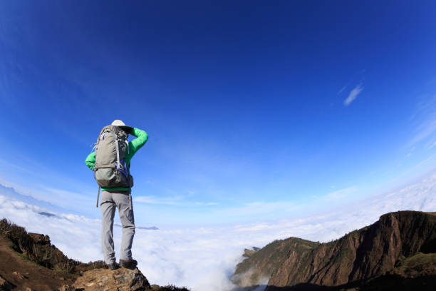 Successful woman backpacker standing on mountain peak cliff edge