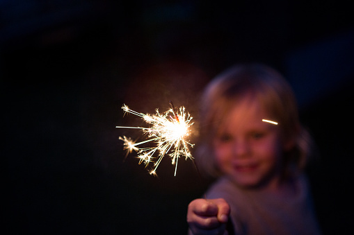 A happy child holds out a sparkler at night