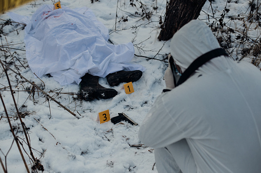 A picture of a forensic photographing evidence at a crime scene in the snow.