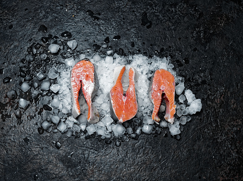 Fresh salmon steaks on ice over black background