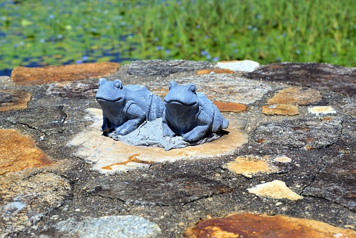 Terracotta figures of frogs sitting on stone wall in garden.