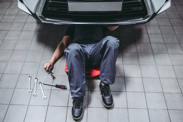 Handsome auto service mechanics. Handsome mechanic in uniform is working in auto service with wrenches. Man on portable plastic repair creeper. Car repair and maintenance. mechanic working under car stock pictures, royalty-free photos & images