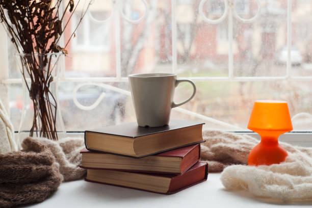 istock Coffee cup, stack of books, lantern and warm scarf on window siil with bokeh. Reading and rest concept. 898492018