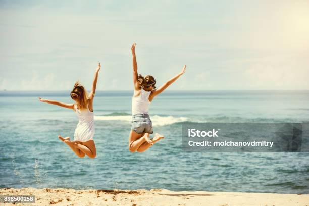 Zwei Glückliche Mädchen Springt Am Sonnenstrand Stockfoto und mehr Bilder von Strand - Strand, Freundschaft, Hochspringen