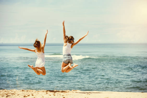 Two happy girls jumps at sunny beach Travel concept with two happy girls jumping at hot sunny beach people jumping sea beach stock pictures, royalty-free photos & images