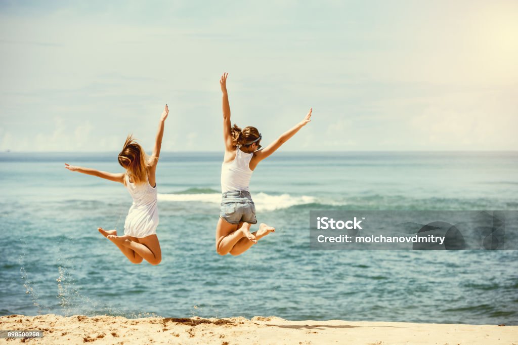 Dois saltos de meninas felizes na praia ensolarada - Foto de stock de Praia royalty-free