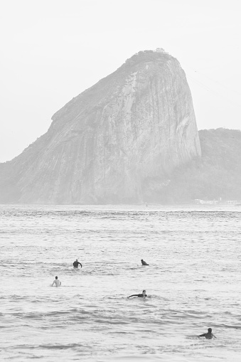 Niteroi, Rio de Janeiro, Brazil. 13th August 2017. Five men surf at the sea in a black and white high key scene. Rough sea at Guanabara Bay with the Sugarloaf Mountain on the background.