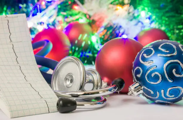 Medical cardiology Christmas and New Year photo - stethoscope and electrocardiogram tape are located near balls for Christmas tree in blurry background with electric garlands lights and toys