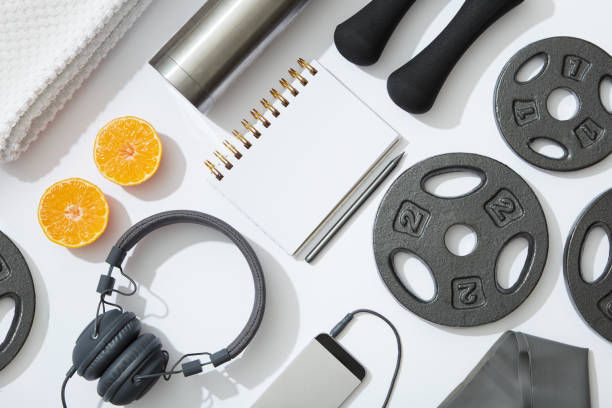 Fitness flat lay, dumbbells, notebook, headphones, notebook, towel on white background