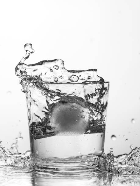 Ice cube drops in a glass of water with a splash
