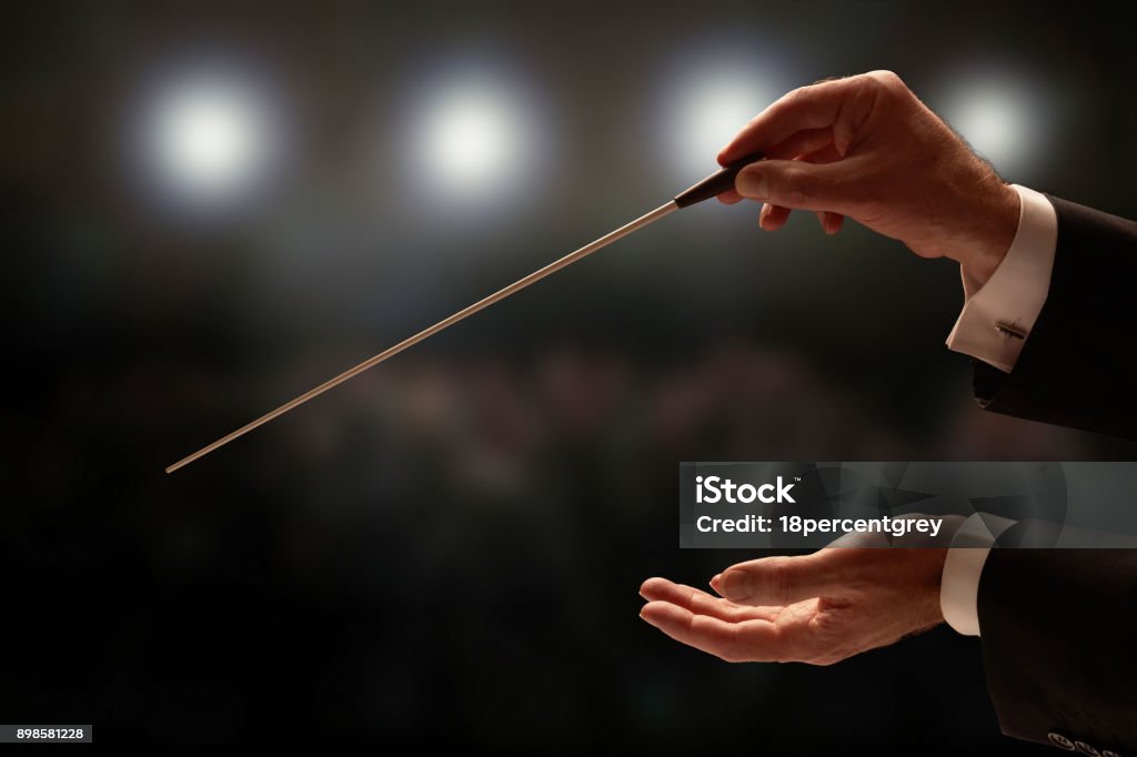 Conductor conducting an orchestra Conductor conducting an orchestra with audience in background Musical Conductor Stock Photo