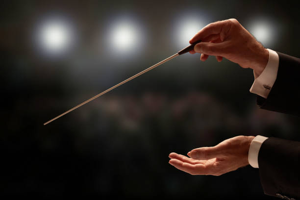 Conductor conducting an orchestra Conductor conducting an orchestra with audience in background musical conductor stock pictures, royalty-free photos & images