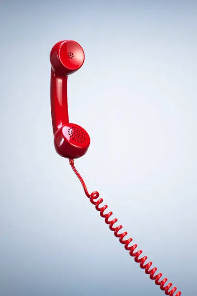 Photo of Red Telephone Receiver with Hanging Cable isolated Beautiful Studio Background.