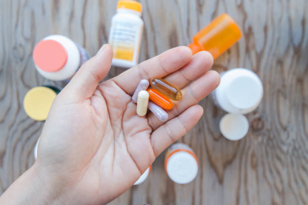 A hand holding a bunch of pills in an open palm. A hand holding a bunch of pills in an open palm. Have are bottles of medicine as a background. nutritional supplement stock pictures, royalty-free photos & images