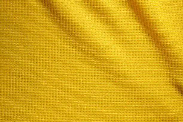 Photo of Sport Clothing Fabric Texture Background. Top View of Cloth Textile Surface. Yellow Football Shirt. Text Space