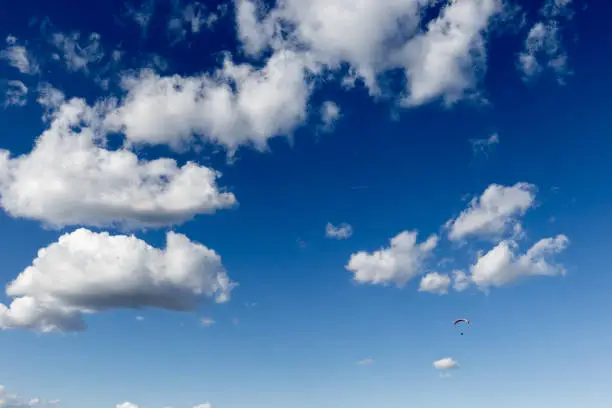 Photo of A paraglider flying against a beautiful deep, blue sky, with big white clouds