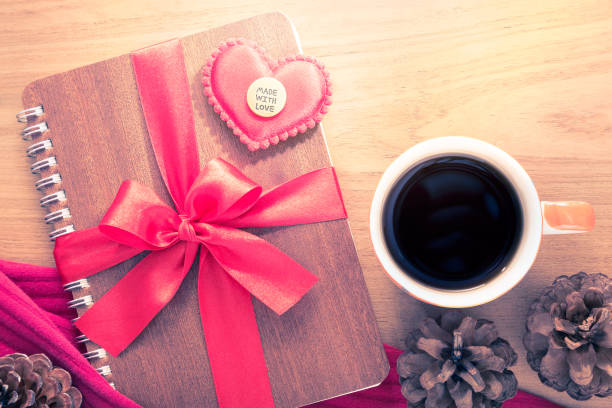 istock Valentine or love theme, felt heart and Made With Love button sitting on notebook wrapped in red ribbon with cup of hot coffee or tea on wooden table, in vintage retro color tone 898679694