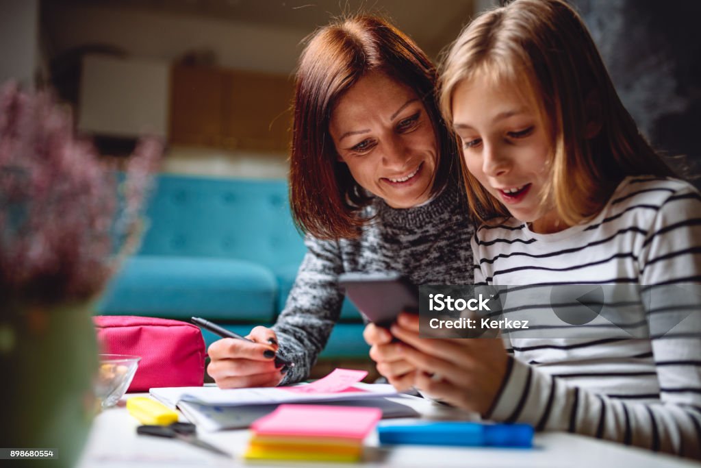 Mother and daughter using smart phone Mother and daughter doing homework late at night and using smart phone Mother Stock Photo