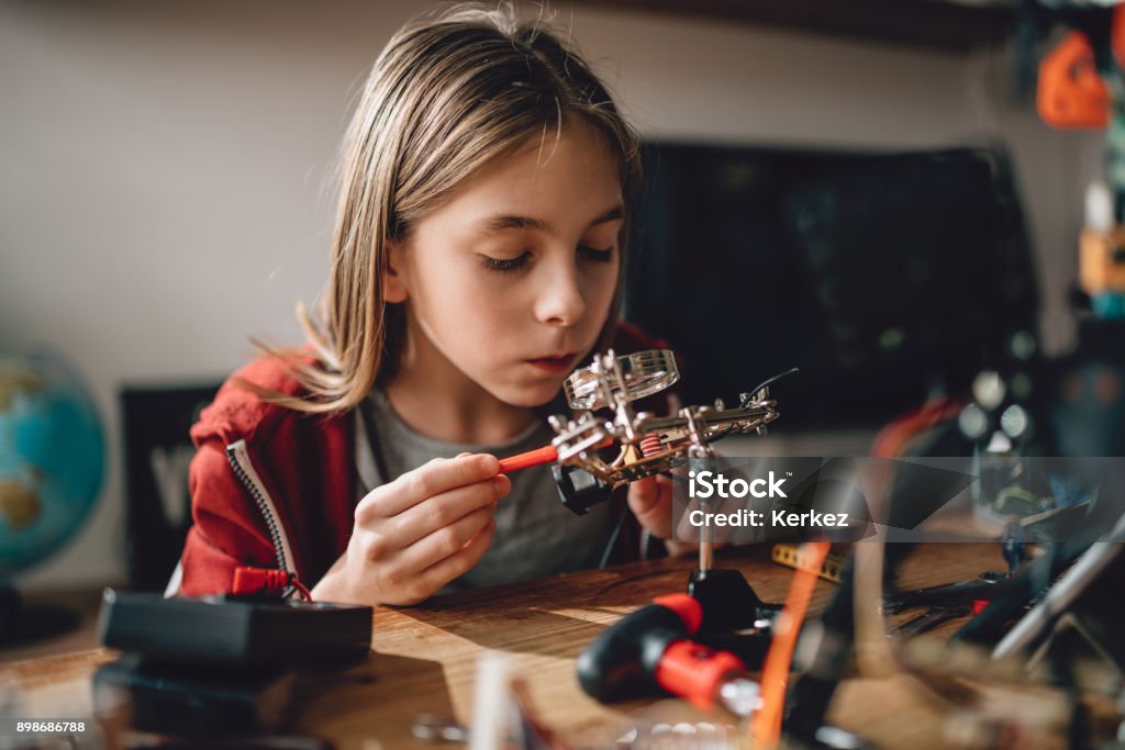 Girl learning robotics Girl wearing red hoodie looking circuit board throughout magnifying glass at home and building a robot Child Stock Photo